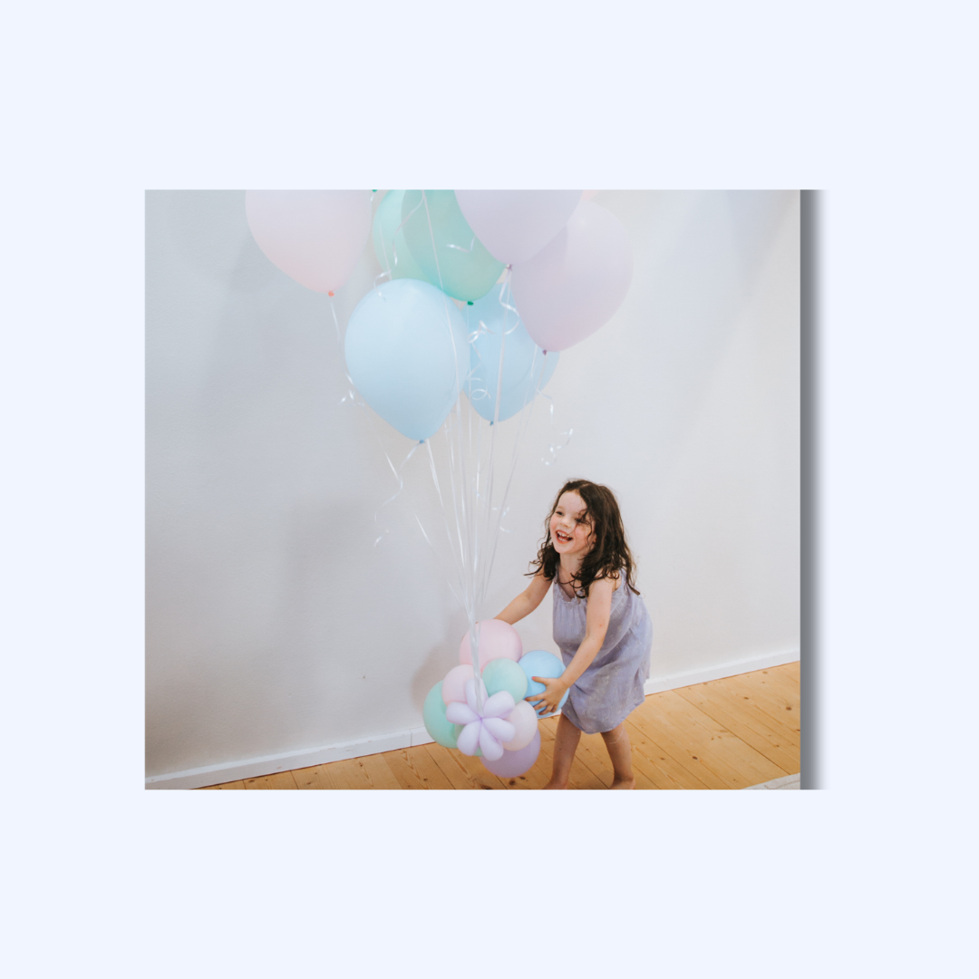 Mädchen spielt mit mehreren Luftballons in Pastellfarben